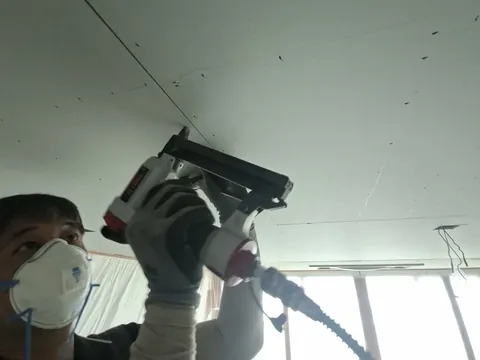 우물천장과 함께 문의하는 석고보드시공, 천장 골조에 석고보드를 타카로 고정하는 작업자